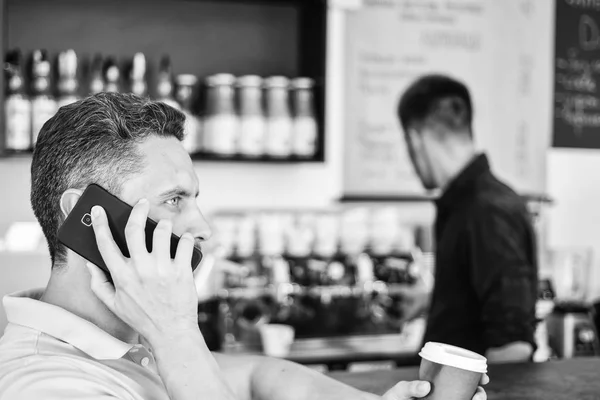 Coffee to go useful option for busy people. Call friend to have drink together. Guy busy speak phone while relax coffee break. Ready to hear you. Man holds cup of drink while have mobile conversation