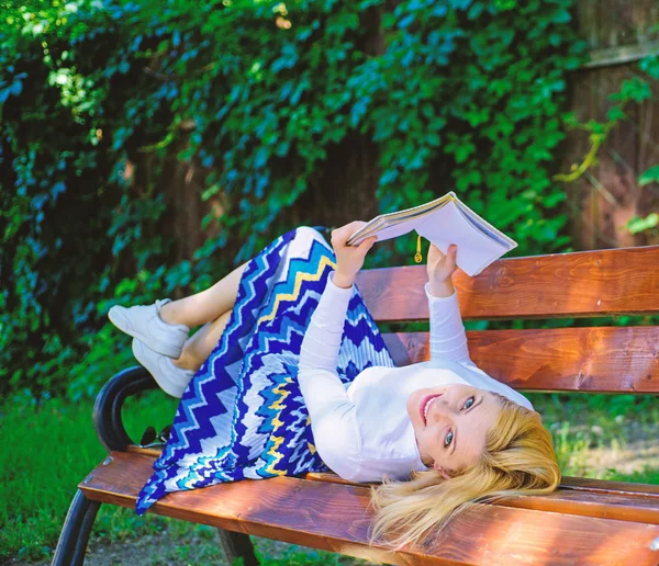 Smart and pretty. Smart lady relaxing. Girl lay bench park relaxing with book, green nature background. Woman spend leisure with book. Interesting book. Girl reading outdoors while relaxing on bench