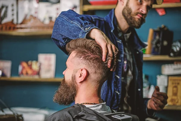 Hipster client with fresh haircut or hairstyle. Barber styling hair of bearded client with wax by hands. Man with beard and mustache in hairdressers chair, shelves on background. Barbershop concept — Stock Photo, Image