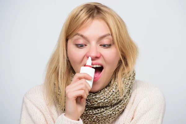 For cold relief. Unhealthy girl with runny nose using nasal spray. Sick woman spraying medication into nose. Cute woman nursing nasal cold or allergy. Treating common cold or allergic rhinitis