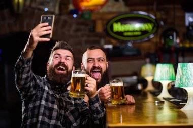Çevrimiçi iletişim. Sakallı hippi adam akıllı telefon tutar. Selfie konseptini alıyorum. Barda harika bir akşam geçirdiğini hatırlamak için selfie çek. Arkadaşların sosyal ağlarına selfie çek. Barda bira içen bir adam
