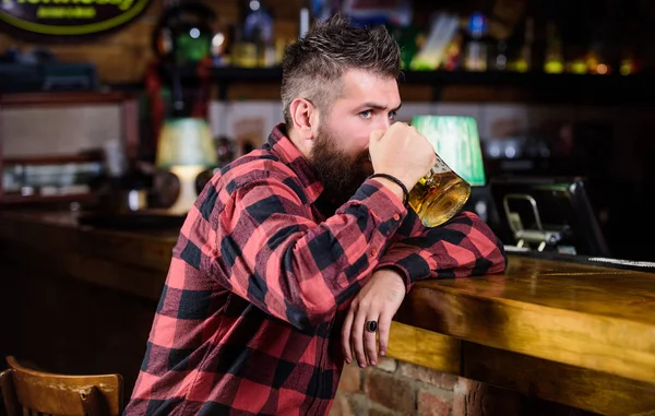 Bar is relaxing place have drink and relax. Man with beard spend leisure in dark bar. Hipster relaxing at bar with beer. Brutal hipster bearded man sit at bar counter drink beer. Order alcohol drink