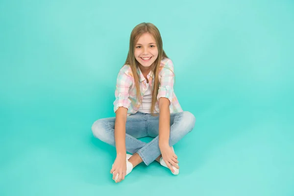 Find place to relax. Girl happy face sit on floor attentive looking at camera turquoise background. Kid girl with long hair relaxing. Just relaxing here. Feel comfortable and freely. Time to relax