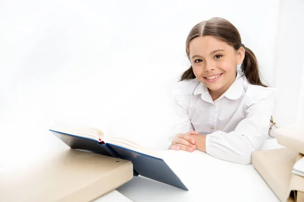 Školačka studium učebnice. Kid školy jednotná šťastný obličej číst knihu. Vzrušený o znalosti. Koncepce knihy. Zajímavá kniha pro děti. Dívka dítě číst knihy sit stůl bílý interiér — Stock fotografie