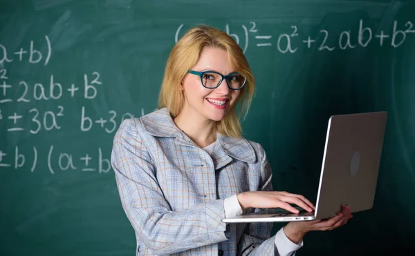 Vzdělávač chytrá chytrá dáma s moderním notebookem vyhledávání informační tabuli pozadí. Nauč se to po dobrém. Koncept digitálních technologií. Žena učitel nosit brýle drží notebook surfování na internetu — Stock fotografie