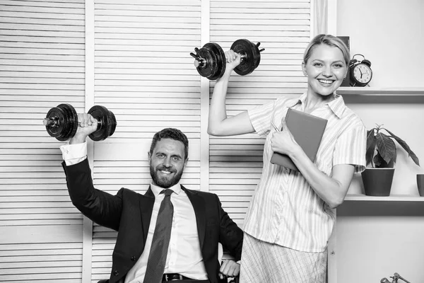 Strong business team. Healthy habits in office. Man and woman raise heavy dumbbells. Strong powerful business strategy. Good job concept. Boss businessman and office manager raise hand with dumbbells