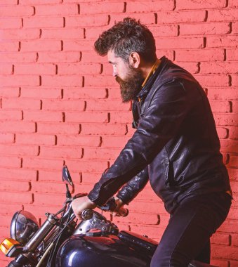 Sakallı, motorcu motorlu bisiklet garaj, tuğla duvar arka plan yakınındaki deri ceketli adam. Yolculuk kavramı başlangıcı. Yenilikçi, vahşi Motorcu deri ceket ciddi yüzüne üzerinde motosiklet üzerinde alır.