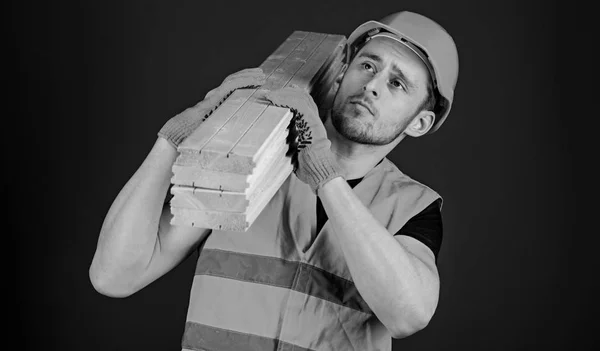 木匠, 木工, 坚强的建设者在周到的面孔运载木横梁在肩膀上。木质材料的概念。男子头盔, 硬帽子和防护手套持有木梁, 蓝色背景 — 图库照片