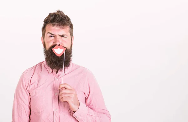 Emotional dissonance concept. Man holding party props smiling lips while his face serious, white background. Hipster with beard and mustache on strict face posing with happy smiling mouth, copy space — Stock Photo, Image