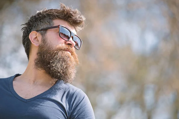 El tipo con barba lleva gafas de sol. Hipster con barba y bigote en la cara estricta, fondo de la naturaleza, desenfocado. El hombre con barba se ve elegante y confiado en el día soleado. Concepto de moda y estilo —  Fotos de Stock