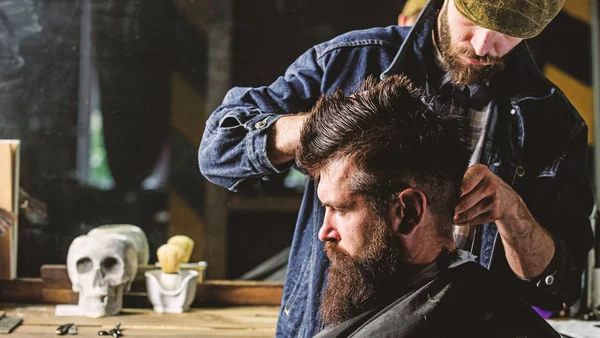 Hipster client getting haircut. Barber styling hair of brutal bearded client with clipper. Barber with hair clipper works on hairstyle for man with beard, barbershop background. Haircut concept — Stock Photo, Image
