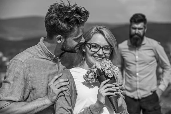 Pareja enamorada citas mientras celoso barbudo hombre viendo esposa engañándolo con amante. Pareja romántica pareja amantes flores ramo. Concepto de infidelidad. Los amantes abrazos al aire libre coquetear relaciones románticas — Foto de Stock