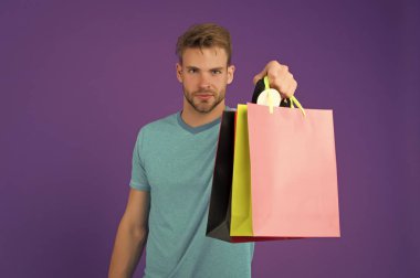 Maço menekşe arka plan üzerinde renkli kağıt torbalar ile. Alışveriş torbaları olan adam. Moda shopper rahat mavi tshirt. Tatil hazırlanması ve kutlama. Alışveriş veya satış ve cyber Pazartesi