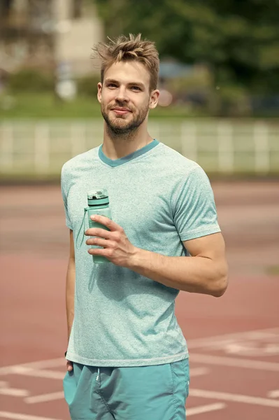 Чоловік зі спортивним виглядом тримає пляшку з водою. Спортсмен п'є воду після тренування на стадіоні в сонячний день. Спортивний і здоровий спосіб життя концепція. Чоловік спортсмен в спортивному одязі тренування на відкритому повітрі — стокове фото