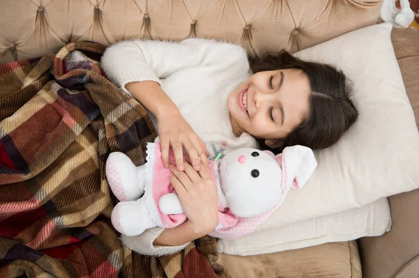 Girl child wear pajamas hug bunny. Play soft toy before go sleep. Sleep with toy. Girl enjoy evening time with favorite toy. Kid lay bed and hug bunny toy couch pillow blanket background top view — Stock Photo, Image