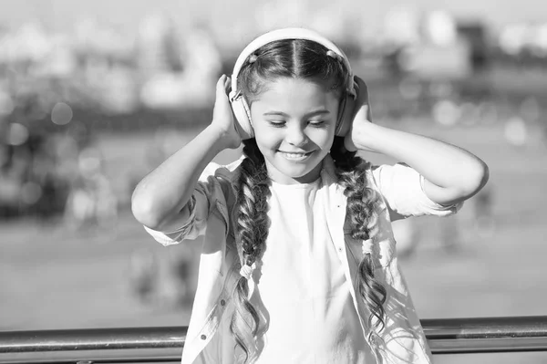 Little girl listening music enjoy favorite song. Girl with headphones urban background. Positive influence of music. Child girl enjoying music modern earphones. Childhood and teenage music taste