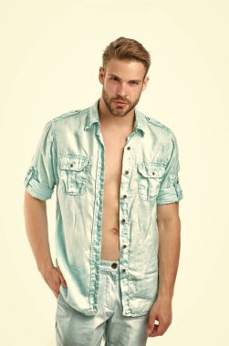 Adam düğmesiz keten mavi gömlekle çekici görünüyor. Sakince poz veren, el ele, beyaz arka planda bir adam. Tüylü adam rahat ya da resmi gömlek giyiyor. Moda konsepti