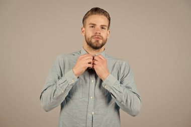 Sakallı adam düğmesi mavi gömlek. Tıraşsız yüzlü sakallı bir adam. Gri arka planda günlük kıyafetli manken. Moda, moda ve moda konsepti. Cilt bakımı ve berber salonu