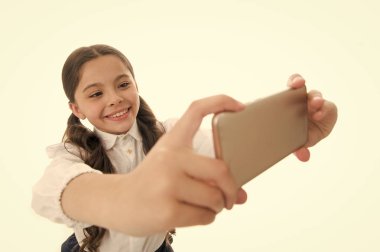 Selfie çekeyim. Şirin, uzun kıvırcık saçlı bir kız akıllı telefon tutuyor ve selfie beyaz arka plan çekiyor. Çocuk okul üniformaları akıllı telefon bulundurur. Çocuk okulu üniforması zeki çocuk gülen surat