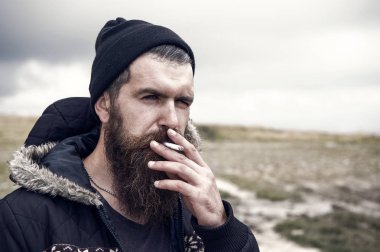 Genç sakallı hippi adam duman sigara Mountain, bulutlu gökyüzü