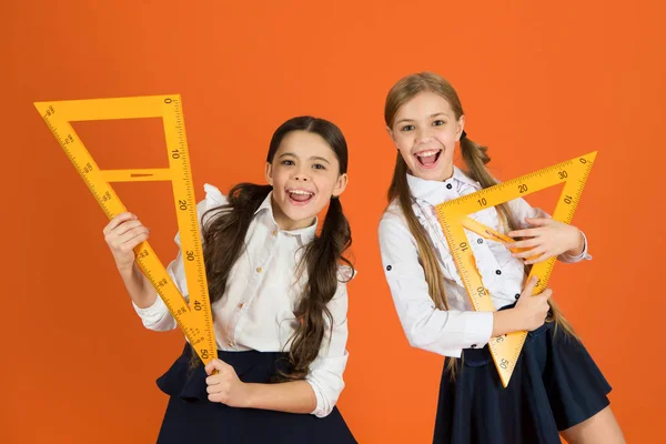 School students learning geometry. Kids school uniform on orange background. Pupil cute girls with big rulers. Geometry school subject. Drawing with ruler chalkboard. Education and school concept — Stock Photo, Image