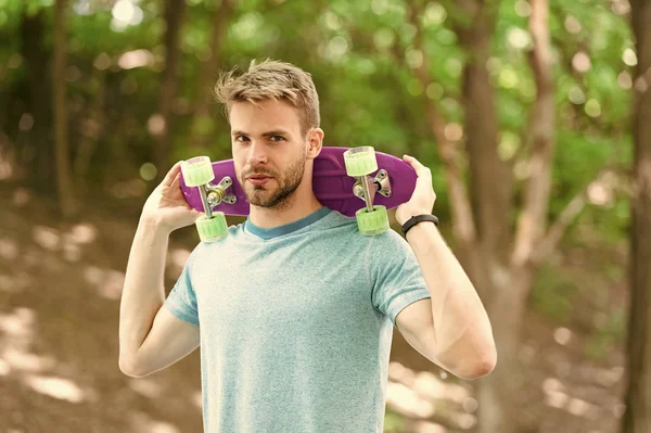 Conceito Hobby. Homem sorridente rosto posando com penny board parque natureza fundo, desfocado. O tipo carrega penny board nos ombros, pronto para andar. Homem gosta de andar de skate e estilo de vida esportivo — Fotografia de Stock