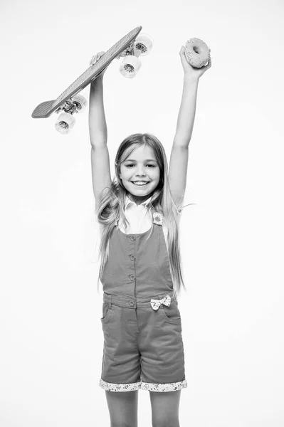 子供女の子はリラックス ホールド ペニー ボードです。アクティブなレジャーの概念。女の子は、白い背景の上のペニーのボードと甘いドーナツを上げます。もともと女の子スケート ボードを設計されています。子供のためのプラスチックの明るいペニー ボード — ストック写真