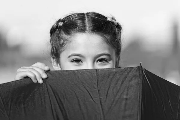 Playing hide and seek. Funny young girl hiding from somebody. Beautiful bright eyes. Girl with umbrella playing game. Having funny mood. Childhood without problems and troubles. Playing outside