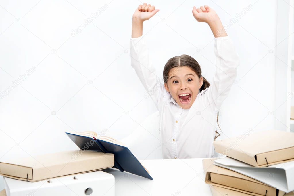 I did it. Happy girl keeping her arms raised at desk. Schoolgirl reading school book. Small child have literature lesson. Little girl reading lesson book in school. Cute pupil develop reading skills