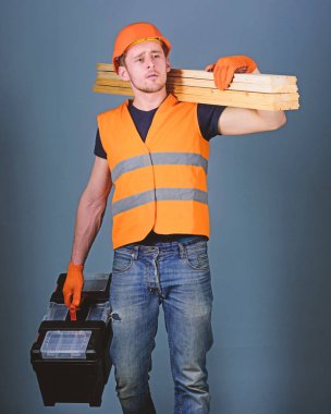 Dostum, tamirci kask, kask içinde tutan araç kutusu ve ahşap kirişler, gri arka plan. Marangoz, woodworker, işçi, rüya gibi yüz taşıdığı ahşap kirişler omuz üzerinde Oluşturucu. Ustalığının kavramı