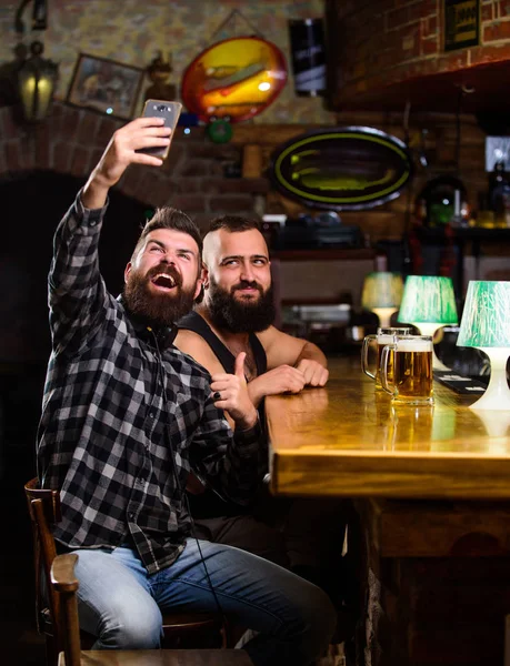 Man in bar drinking beer. Take selfie photo to remember great evening in pub. Online communication. Man bearded hipster hold smartphone. Taking selfie concept. Send selfie to friends social networks.