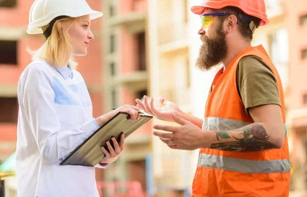 Safety inspector concept. Woman inspector and bearded brutal builder discuss construction progress. Construction site safety inspection. Discuss progress project. Construction project inspecting