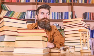 Kitap kurdu kavramı. Katı yüz sit Kitaplığı'nda, eğitim sırasında kitaplar, kitap rafı arka plan üzerinde yığınları arasında adam. Öğretmen veya tablo ile kum saati ve defocused gözlük, sakal oturup ile öğrenci