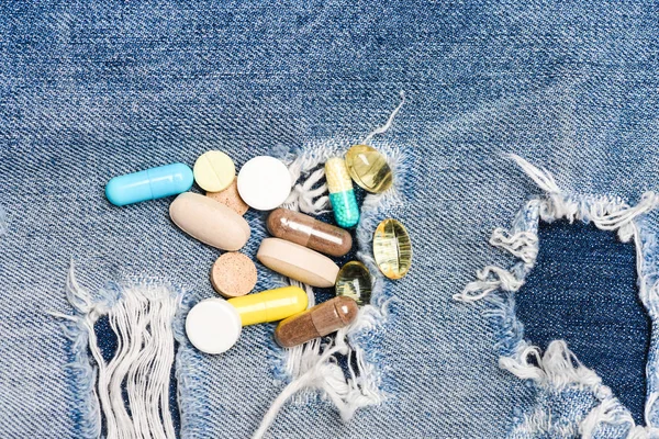 Наркомания. Концепция медицины и лечения. Наркотики на фоне джинсов. Набор красочных таблеток. Смешивание лекарств. Быстрое лечение. Рецепт лекарства. Здравоохранение и болезни. Доза и зависимость — стоковое фото