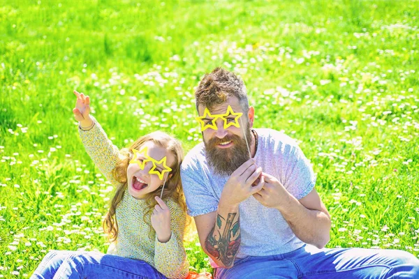 Концепція рок-зірки. Батько і дочка сидять на траві на траві, на зеленому тлі. Дитина і тато позують з атрибутом фотокамери у формі зірок на лузі. Родина проводить дозвілля на відкритому повітрі — стокове фото