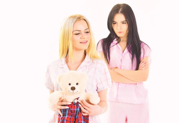 Ревность и зависть. Сестры в пижаме выглядят недружелюбными, ревнивыми. Девушки в розовой пижаме, на изолированном белом фоне. Леди ревнует к сестре плюшевого игрушечного медведя, обезжиренного — стоковое фото