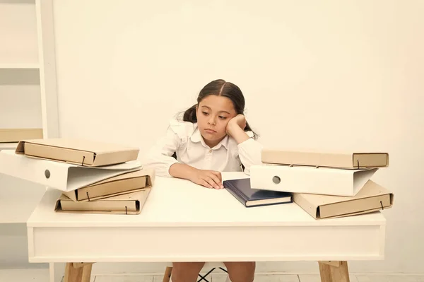 Demasiado para aprender. Menina criança cansada exausta sentar-se à mesa perto de pilha de livros fundo branco. Estudante cansado de estudar e ler livros. Kid escola uniforme cansado rosto não quer continuar lendo — Fotografia de Stock