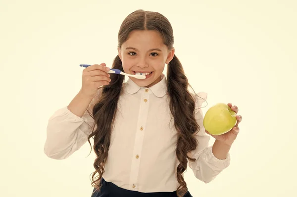 Munhygien. Flicka söt håller tandborste och äpple vit bakgrund. Barn flicka håller äpple och borste tand med pasta. Barn skolflicka smart unge glad ansikte bryr hygien. Borsta tänderna koncept — Stockfoto