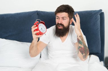 Çalar saat ile kaldırın. Yine uyuya kalmışım. Erken uyanma için ipuçları. Erken bir yükseltici olmak için ipuçları. Adam hipster uykulu yüz ile çalar saat yatakta sakallı. Sabah erken uyanma ile sorun