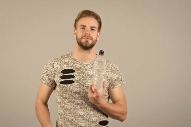 Adam atletik çekici görünüm su şişesi tutar. Adam atlet casual giyinen umurunda hidrasyon, gri arka plan hakkında. Sağlıklı yaşam konsepti. Adam sakin yüz suyu sportif şişeden içer.