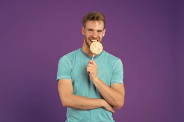 Lolipop menekşe arka plan üzerinde mutlu adam. Maço gülümseme şeker mor zemin üzerinde sopa ile. Girdap karamel ile mavi tshirt moda modeli. Yemek veya aperatif ve tatlı yeme. Punchy pastel