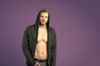 Sakallı adam menekşe arka planda kapüşon takıyor. Sıradan tişörtlü, seksi vücutlu bir maço. Kapüşonlu manken. Aktif yaşam tarzı ve sağlık aktiviteleri. Moda tarzı ve trend konsepti, alanı kopyala