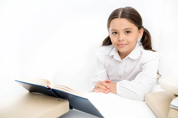 女童读书坐桌子白色的内部。学习课本的女学生。孩子校服快乐的脸读书。对知识感到兴奋。在家上学的概念。有趣的书为孩子 — 图库照片