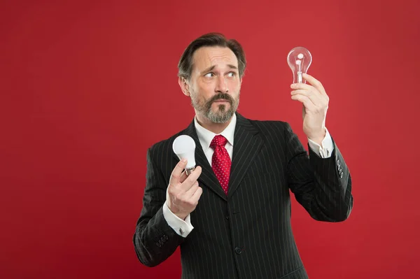 Lighting choices to save money. Man bearded consultant formal suit hold light bulb on red background. Symbol of idea progress and innovation. Environment friendly lighting. Energy efficient lighting — Stock Photo, Image