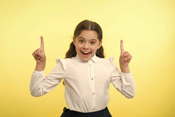Lilla geniet har en idé. Lycklig flicka hålla fingrarna upp på gul bakgrund. Tillbaka till skolan. Ett litet leende med inspiration. Vilken bra idé. Bara inspirerad. Sorglös skönhet — Stockfoto
