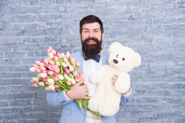 Hombre romántico. Macho preparándose cita romántica. Esperando a mi amor. Hombre bien arreglado llevar esmoquin pajarita sujetar flores tulipanes ramo y juguete oso de peluche grande. Invítala a salir. Regalo romántico — Foto de Stock