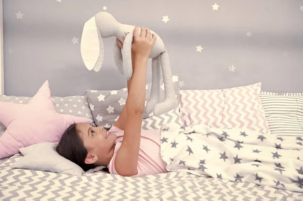 Mejores amigos. Niña acostada en la cama con juguete gris conejito en su dormitorio. El chico se prepara para ir a la cama. Desea dulces sueños a tu juguete favorito. Chica niño relajarse y jugar conejito juguete antes de conciliar el sueño — Foto de Stock