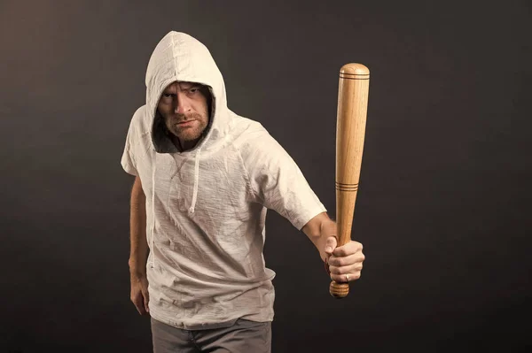 Man hold baseball bat, agression. Hooligan wear hood in hoody, fashion. Gangster guy threaten with bat weapon. Aggression, anger and violence concept