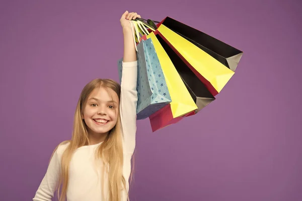 Szczęśliwe dziecko z torby papierowe. Mała dziewczynka uśmiech z torby na zakupy na fioletowym tle. Dzieciak shopper w na fioletowym tle. Przygotowaniu wakacje i uroczystości. Zakupy i sprzedaż na czarny piątek — Zdjęcie stockowe