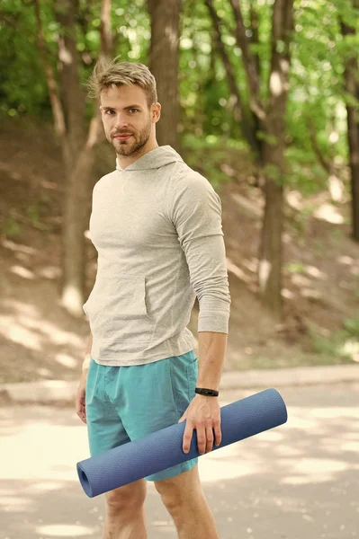 Praticar ioga. Sportsman carrega tapete de ioga para praticar ao ar livre. Conceito de ioga exterior. Homem atleta no rosto sorridente carrega tapete, indo para alongamento, fundo da natureza. Atleta com rastreador de fitness — Fotografia de Stock